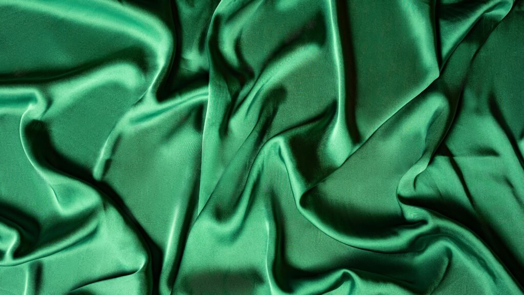 Close-up of crumpled emerald green silk fabric creating a smooth, luxurious texture.