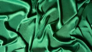 Close-up of crumpled emerald green silk fabric creating a smooth, luxurious texture.
